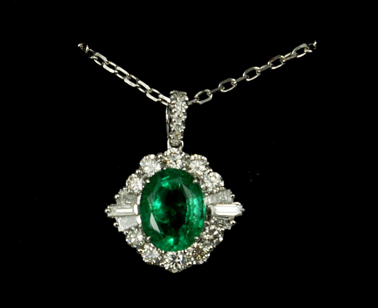 AN 18CT WHITE GOLD OVAL EMERALD AND DIAMOND CLUSTER PENDANT on an 18ct white gold chain. (Approx