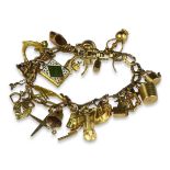 A 9CT GOLD CHARM BRACELET Hung with various 9ct gold charms including dice, a revolver, cello,