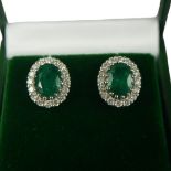 A PAIR 18CT WHITE GOLD OVAL EMERALD AND DIAMOND CLUSTER STUDS. (Emeralds 2.67ct, Diamonds 0.61ct),