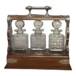 A 19TH CENTURY SILVER PLATED OAK AND CUT GLASS THREE BOTTLE TANTALUS Having a single carry handle,