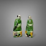 An attractive Pair of Biscuit Figures, Kangxi, both on a rectangular 'egg and spinach' enamelled