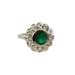 A WHITE METAL, EMERALD AND DIAMOND CLUSTER RING Having a round cut emerald edged with round cut