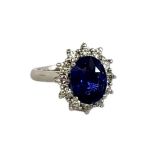 A PLATINUM, SAPPHIRE AND DIAMOND CLUSTER RING Having an oval cut sapphire edged with round cut