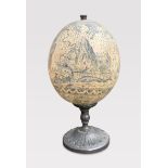 AN EARLY 20TH CENTURY FAUX SCRIMSHAW OSTRICH EGG UPON STAND. (h 22cm)