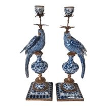 A PAIR OF CONTINENTAL BLUE AND WHITE FIGURAL CANDLESTICKS The bronze sconces above seated parrots