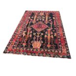 A PERSIAN WOOLLEN RUG Having floral motifs to central field on black ground and three running