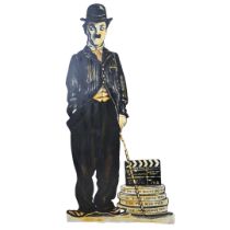 A LARGE WOODEN HAND-PAINTED THEATRE PROP, FIGURE OF CHARLIE CHAPLIN AS ‘THE TRAMP’ Stood beside a