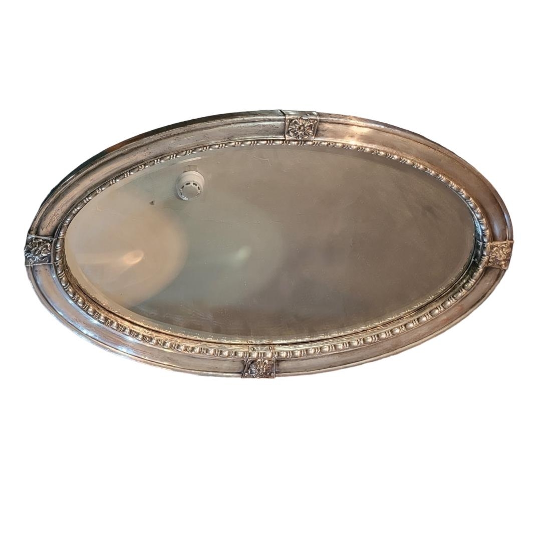 AN ARTS AND CRAFTS SILVER PLATE ON COPPER OVAL MIRROR With applied florets, shaped border and