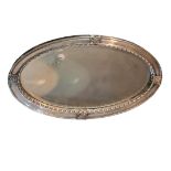 AN ARTS AND CRAFTS SILVER PLATE ON COPPER OVAL MIRROR With applied florets, shaped border and