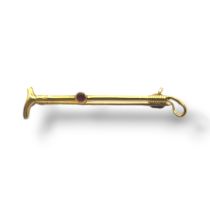 AN EARLY 20TH CENTURY YELLOW METAL AND GARNET 'RIDING CROP' BAR BROOCH Set with a single round cut
