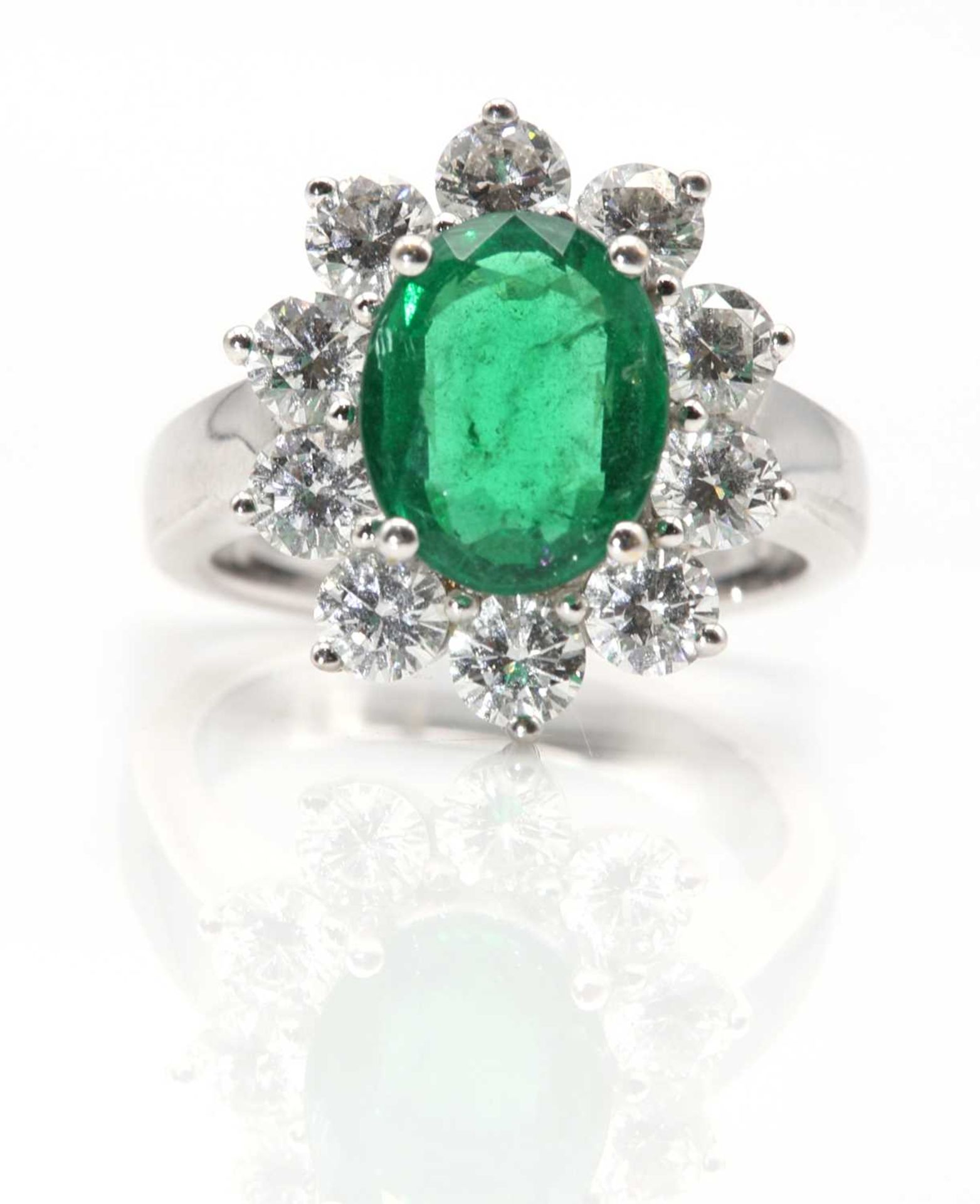 An 18ct white gold Zambian emerald and diamond oval cluster ring,