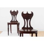 A pair of George III mahogany 'pelta-back' hall chairs,