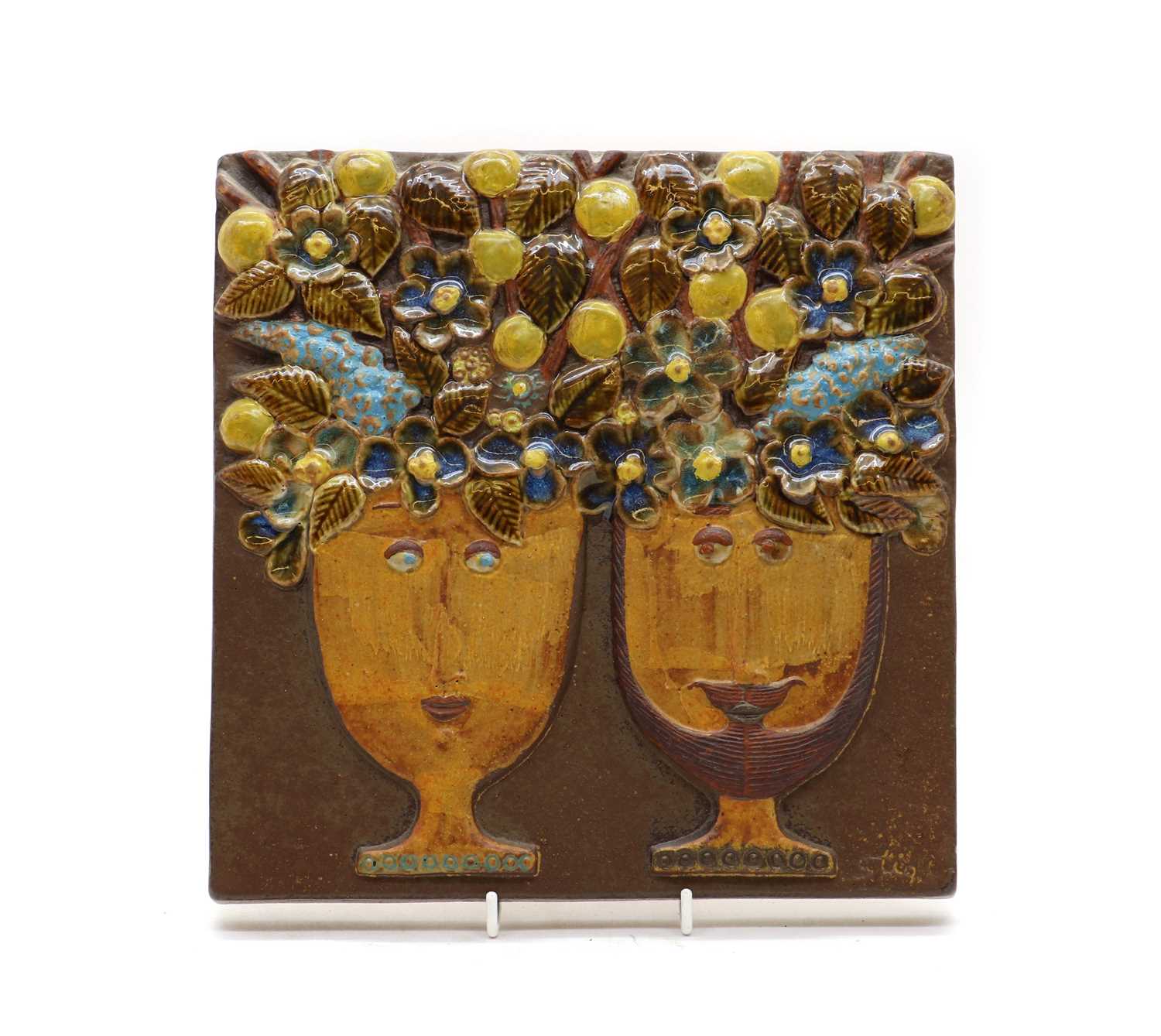 A Gustavsberg glazed wall plaque, Stig Lindberg, depicting two heads on cups, with fruit and leaves,