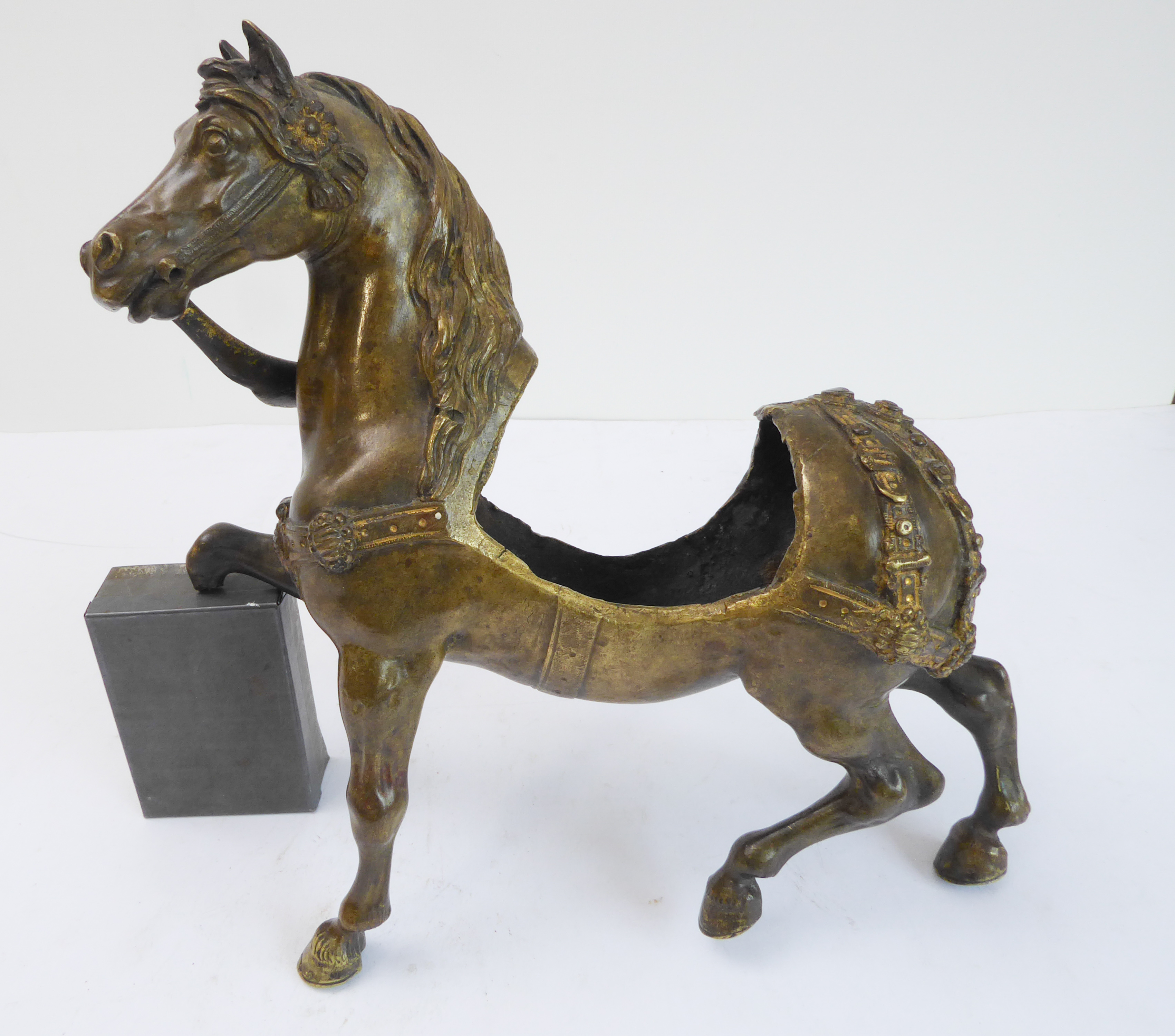 A bronze sculpture of a horse with decorative cast harness and open saddle section (saddle, leg