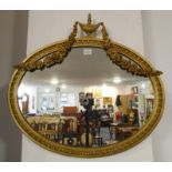 An oval gilt-framed wall-hanging looking glass in neoclassical style, surmounted with an urn and