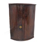 An unusual mid 18th century bow-fronted hanging oak corner cupboard: with original blacksmith made