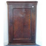 An 18th century hanging oak corner cupboard: the single panelled door with H-form hinges and opening