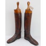 A pair of post-war brown-leather riding boots with wooden trees.The left boot is a bit scuffed,