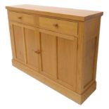 A modern light oak side cabinet; two half-width drawers above two panelled doors and raised on