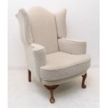 A good oatmeal-coloured upholstered wing-backed armchair in early style: raised on walnut turned