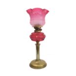 A 19th century brass and cranberry glass oil lamp: the large crimped shade above a faceted cranberry