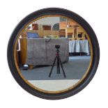 A large circular wall-hanging looking glass with parcel-gilt ebonised frame. (John Lewis &