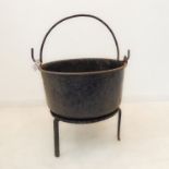 An early and large iron cooking pot with arched handle, raised upon an early trivet (52 cm wide)