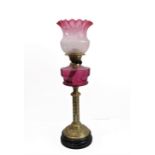 A 19th century brass-mounted oil lamp with cranberry glass reservoir and crimped shade: foliate