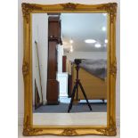 A modern gilt-framed wall-hanging looking glass; outset corners and hand-bevelled plate (frame