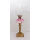 A 19th century glass and brass oil lamp: foliate style decorated spherical glass shade and cranberry