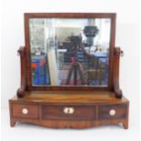 An early 19th century bow-fronted mahogany toilet mirror: the rectangular plate flanked by scrolling