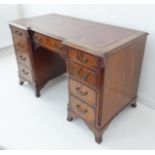 A mid 20th century reproduction inverted breakfront walnut pedestal desk: the conforming gilt-tooled