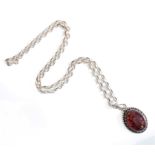 An oval silver pendant with beaded edge around mounted amber polished en cabochon, together with