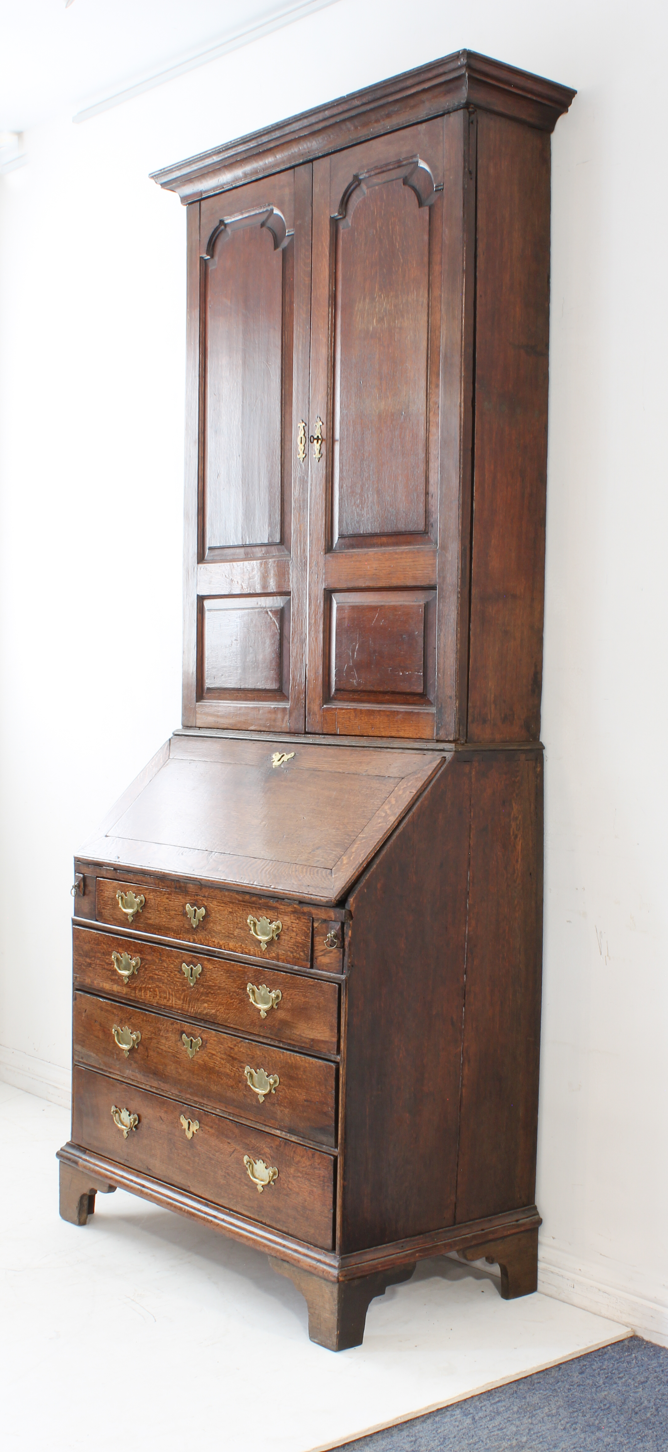 A mid-18th century oak bureau-cabinet: two high fielded panel doors opening to reveal shelves;