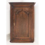 A late 18th century hanging oak corner cupboard: single panel arch-topped door opening to reveal