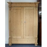 An antique stripped-pine French armoire: inverted breakfront cornice above panelled doors