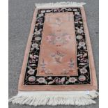 A small Chinese pink ground wool rug: with floral medallion and spandrels, within a black border
