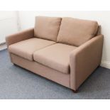 A modern two-seater sofa upholstered in light-coffee fabric and on short square tapering wooden legs