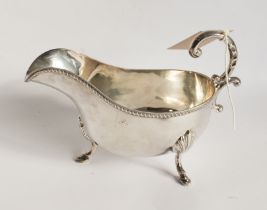 A heavy hallmarked silver sauceboat; high arch scrolling handle above a gadrooned border and three