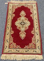 A Kashmir rug; red ground with ivory central medallion (125 x 66 cm).