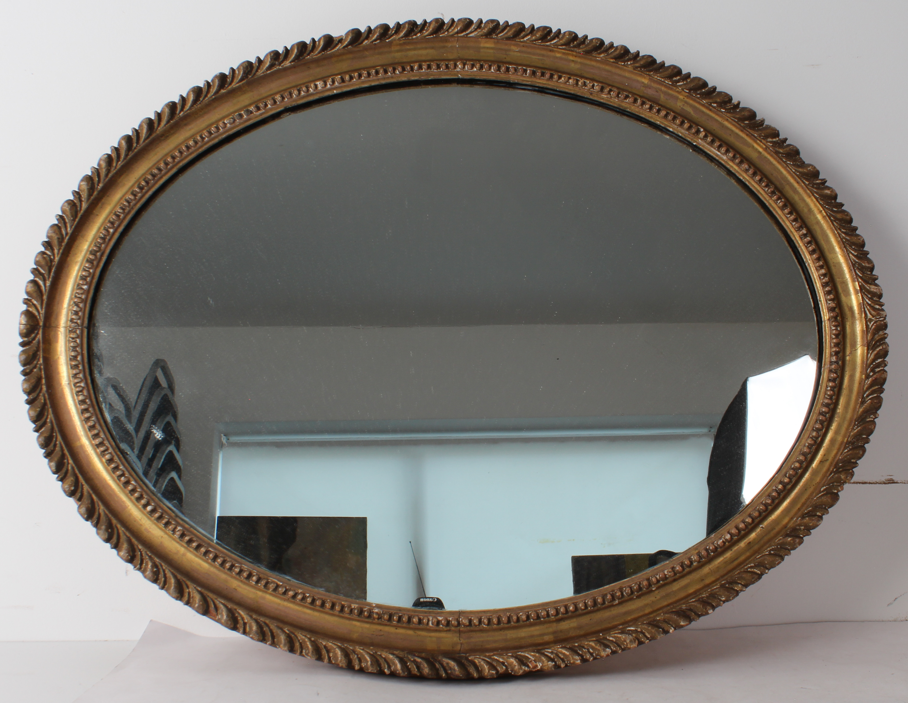 An oval gilt and composition mirror - the late 19th century frame with gadrooned border and shot