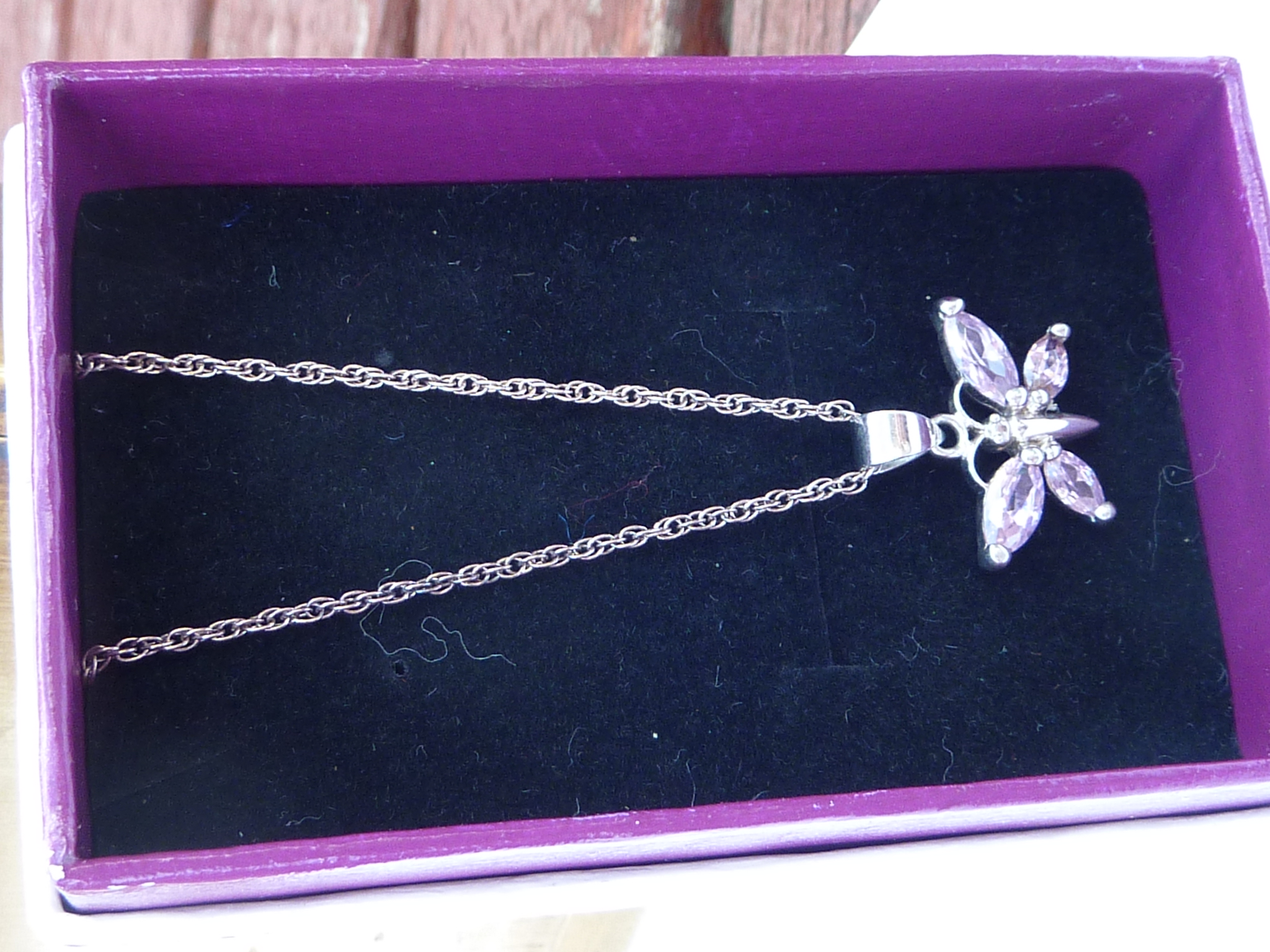 A boxed silver pendant modelled as a butterfly with hand-cut pink stones upon a silver chain.