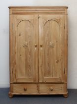 A Victorian pine wardrobe: with two arched panelled doors with applied cartouche decoration