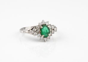 An 18ct white gold, emerald and diamond cluster ring - London hallmarks, the central oval cut