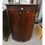 19TH CENTURY MAHOGANY BOW FRONT CORNER CABINET WITH SHELVED INTERIOR BEHIND 2 PANEL DOORS.