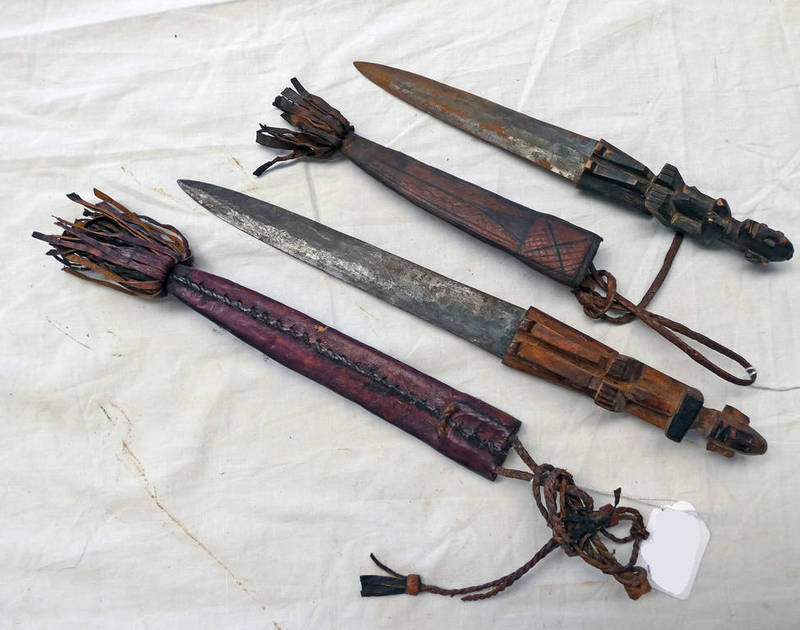 TWO TRIBAL DAGGERS WITH CARVED WOODEN GRIPS IN THE FORM OF MALE AND FEMALE FIGURES WITH LEATHER