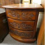 BOWFRONT TEAK CHEST OF DRAWERS WITH CARVED DECORATION.