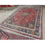 IRANIAN CARPET RED GROUND WITH A MULTICOLOURED BORDER FROM THE MASHHAD REGION OF IRAN 290 X 390CM