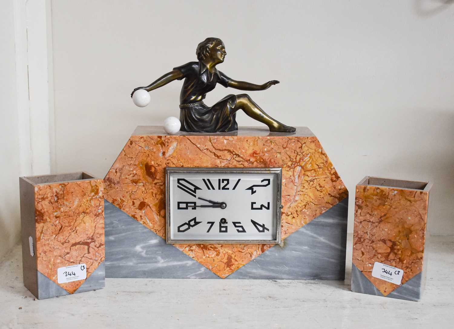 An Art Deco Marble Clock, surmounted with a bronze figure of a seated girl bowling, with