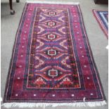 A Baluch Rug, the indigo field with four serrated medallions enclosed by claret borders, 210cm by